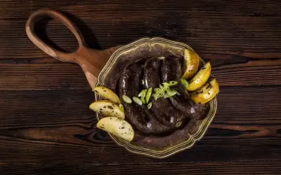 Kaszanka z piekarnika podana z pieczonymi ziemniakami i szczypiorkiem na ozdobnym talerzu.