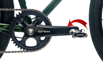 Czerwona strzałka pokazuje kierunek obrotu, by dowiedzieć się, jak odkręcić pedały w rowerze. Widoczny mechanizm korbowy Shimano GRX.