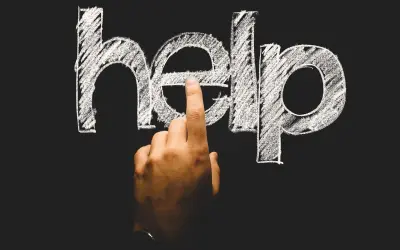 Palec wskazuje literę "e" w napisie "help" na tablicy. To symboliczne wezwanie o pomoc, często pojawiające się w kontekście psychologii rozwojowej.
