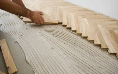 Pose de parquet en chevrons avec de la colle. L'espace entre mur et parquet stratifié est visible.