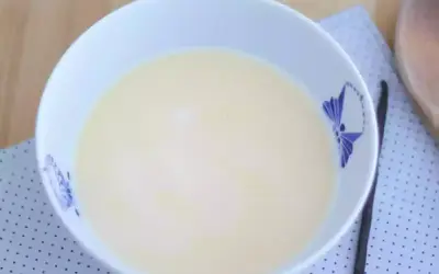 En skål med krämig vaniljsås, perfekt för ditt vaniljsås recept. En vaniljstång ligger bredvid.