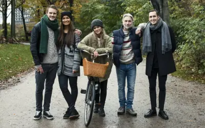 Pięcioro przyjaciół w jesiennych stylizacjach, przykład szwedzkiego stylu ubierania. Jeden z nich ma rower z wiklinowym koszykiem.