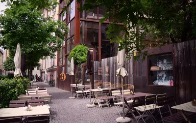 Tavoli all'aperto e ombrelloni di fronte al Batzen Bräu, con un'architettura industriale e un'atmosfera rilassata.