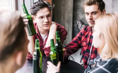 Młodzi ludzie przy stole, butelki piwa, początek alkoholizmu wśród młodzieży.