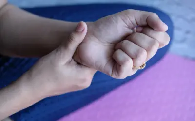Dłoń z pierścionkiem uciska nadgarstek, sugerując uczucie mrowienia lub drętwienia, czyli parestezje.