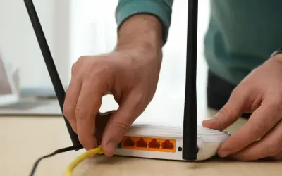 Ręka podłącza żółty kabel do routera. Dowiedz się, jak wzmocnić sygnał wifi domowym sposobem, by cieszyć się lepszym zasięgiem.