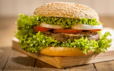 Soczysty burger z wołowiny, sałatą, pomidorem i cebulą w bułce do hamburgerów z sezamem. Idealny pomysł, co zrobić z bułki do hamburgerów.
