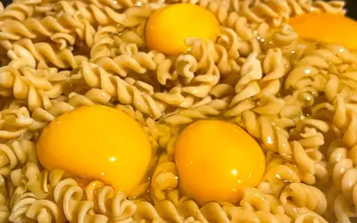 Makaron z jajkiem w trakcie gotowania. Trzy żółtka otoczone przez skręcone nitki makaronu, tworzące apetyczny obraz.