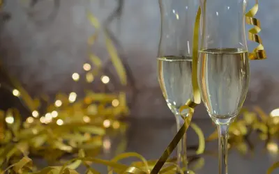 Dwa kieliszki szampana, złote serpentyny i migoczące światełka tworzą atmosferę noworocznych przesądów i celebracji.
