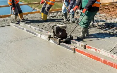 Budowlańcy używają wibrołaty do wyrównania świeżego betonu na budowie.
