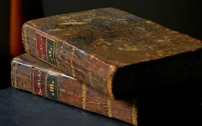 Dwie stare, skórzane księgi, jedna na drugiej. Na grzbietach widoczne napisy, sugerujące zawartość, być może mądrość Salomona z Biblii.