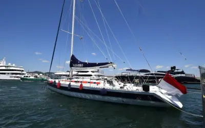 Barca a vela "Nababbo" con bandiera rossa e bianca, in porto con altre imbarcazioni. Sembra una cometa 12.