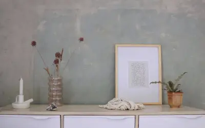 Un tavolino con candela, vaso di fiori secchi, quadro e corda. Sembra la preparazione calce per imbiancare, con un tocco artistico.