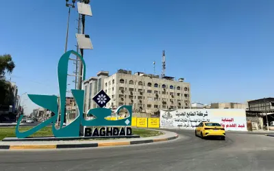 Wielki napis "BAGHDAD" i stylizowany napis arabski na tle budynków i nieba. Stolica Iraku wita podróżnych.