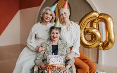 Eleganckie stylizacje na urodziny w lokalu. Trzy kobiety świętują 60. urodziny, otoczone prezentami i złotymi balonami.