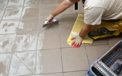 Pracownik usuwa nadmiar fugi epoksydowej z płytek. Wady fugi epoksydowej mogą wynikać z nieprawidłowego wykonania.