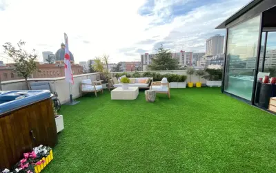 Terraza con césped artificial verde, jacuzzi, muebles de exterior y vistas urbanas. Ideal para aprender como limpiar césped artificial terraza.