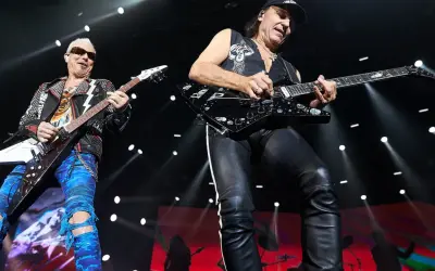 Dwóch gitarzystów na scenie, jeden w skórzanej kurtce i niebieskich spodniach, drugi w czarnej kamizelce i skórzanych spodniach. Ich gra wywołuje "wind of change" tłumaczenie.