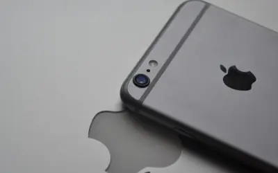 Srebrny iPhone leży na tle z wyciętym logo Apple, symbolizując spójność ekosystemu Apple.