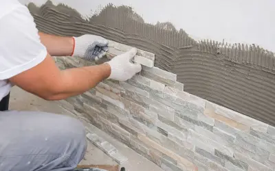 Pose de pierre de parement sur un mur avec du mortier. Un artisan pose méticuleusement les pierres pour un revêtement mural naturel.