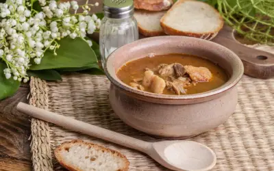 A rustic bowl brimming with the najlepsza zupa gulaszowa, accompanied by crusty bread slices and a wooden spoon.