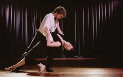 Para tańczy tango na scenie, kobieta w czarnej sukni w głębokim ukłonie, mężczyzna w białej marynarce.