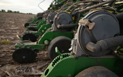 A row of green planters sits in a field, ready for planting. These machines are essential for farmers, contributing to the average hours on a tractor per year.