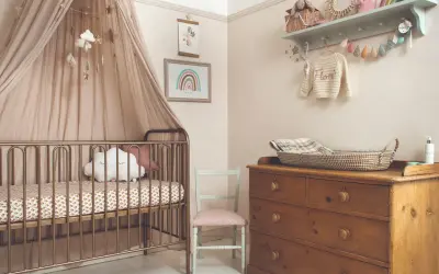 A serene modern nursery theme with a gold crib, cloud mobile, and rainbow art. A vintage dresser holds a woven basket, completing the cozy, dreamy atmosphere.