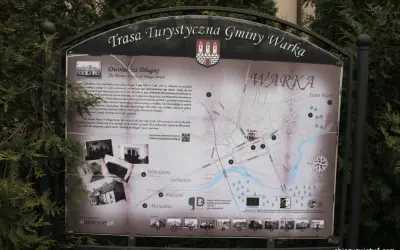 Mapa turystyczna gminy Warka z zaznaczonymi zabytkami, w tym Dworkiem na Długiej. W tle drzewa, a na dole strony logo "Warka" i adres strony.