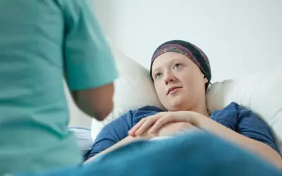 Młoda pacjentka w chustce na głowie leży w łóżku, słuchając pielęgniarki. To może być początek walki z chorobą, gdzie rak przedinwazyjny co to znaczy, jest kluczowym pytaniem.
