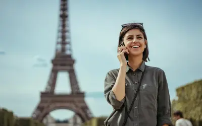 Uśmiechnięta kobieta rozmawia przez telefon w Paryżu, niedaleko Wieży Eiffla. Dowiedz się, jak uruchomić roaming w Play, by cieszyć się rozmowami za granicą.