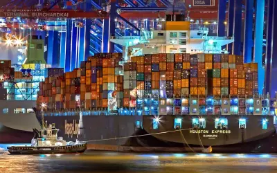 Nocą w porcie holownik pomaga wielkiemu kontenerowcowi. Spedytor, kto to? To osoba organizująca transport.