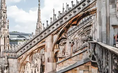 Gotycka architektura Duomo, z której słynie Mediolan, z detalami rzeźb i iglicami na tle błękitnego nieba.