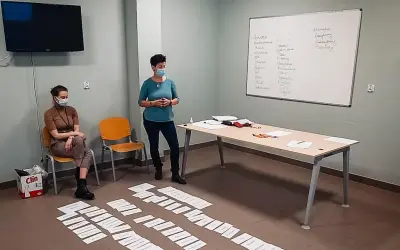 Trening zastępowania agresji: dwie kobiety w maseczkach, tablica z zapiskami, kartki na podłodze.