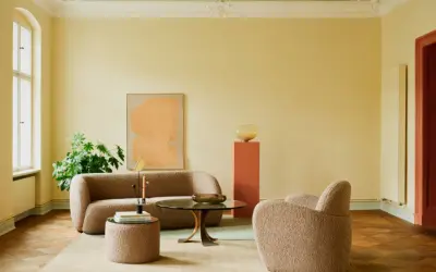 Ein Wohnzimmer mit gelben Wänden und einer grünen Decke, die frisch gestrichen wurde. Ein beiger Teppich, ein Sofa und ein Sessel laden zum Entspannen ein.