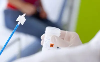 Ręka w rękawiczce trzyma pojemnik na próbkę do cytologii płynnej. W tle widać pacjentkę.