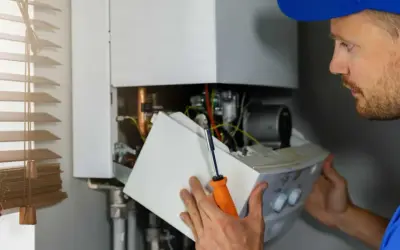 Un technicien examine l'intérieur d'une chaudière à gaz. Il tient un tournevis et une partie de l'appareil.