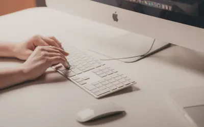 Mani che digitano su tastiera bianca, vicino a un mouse. Attenzione ai sintomi di tendinite da mouse per evitare dolori.