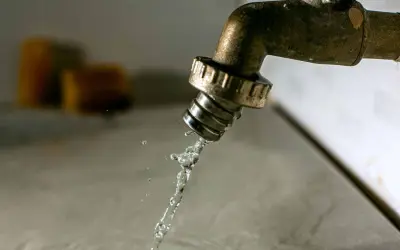 Un robinet en laiton coule, projetant un jet d'eau. Des éponges floues sont visibles en arrière-plan. Il est temps d'avoir plus d'eau dans la maison.