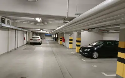 Wrocław główny parking cennik: podziemny parking z białym i czarnym Volkswagenem, białym BMW, rurami i klimatyzacją.