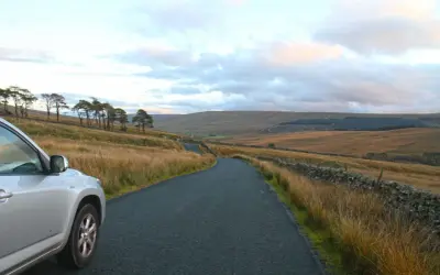 Voiture argentée sur une route sinueuse dans un paysage vallonné. La conduite à gauche est visible sur le côté de la route.