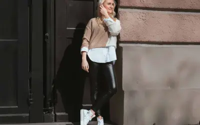Styling-Tipp: So kannst du lederleggings kombinieren. Eine Frau mit blonden Haaren trägt sie mit einem weißen Hemd und einem zweifarbigen Pullover.