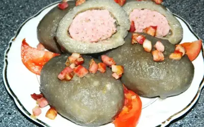 Cepelin z mięsem, polany skwarkami i podany z pomidorem. Wyglądają jak małe cepeliny na talerzu.
