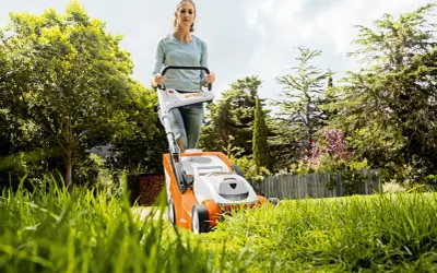 Mujer cortando césped con cortacésped eléctrico. Consejos para cortar el césped: mantén la cuchilla afilada y la altura adecuada.