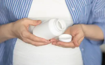 Kobieta w ciąży trzyma białą buteleczkę i jej nakrętkę. Rozważa, czy wziąć paracetamol w ciąży.