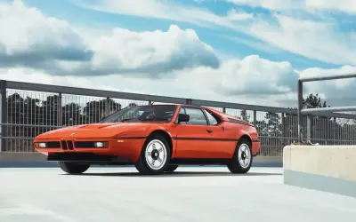 Pomarańczowy klasyk BMW E26 na tle nieba z chmurami.