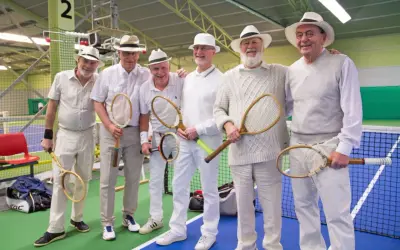 Sex äldre herrar i hattar och vita kläder poserar med tennisracketar, redo för en match i stil med Gustaf V:s tennis.
