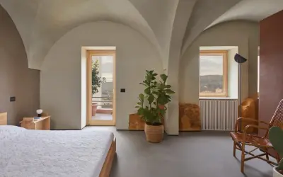 Interno moderno con soffitti a volta, letto, pianta e vista panoramica. Sembra una di quelle case a un euro che diventano gioielli.