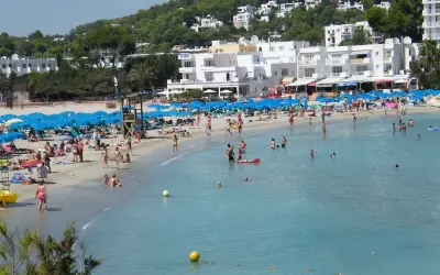Lloret de Mar, lipiec: słoneczna pogoda zachęca do plażowania. Tłumy ludzi kąpią się i opalają na piaszczystej plaży, pod błękitnymi parasolami.