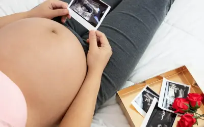 Kiedy widać brzuch ciążowy, przyszła mama trzyma zdjęcie USG. Obok leży pudełko z kolejnymi zdjęciami i czerwonymi różami.